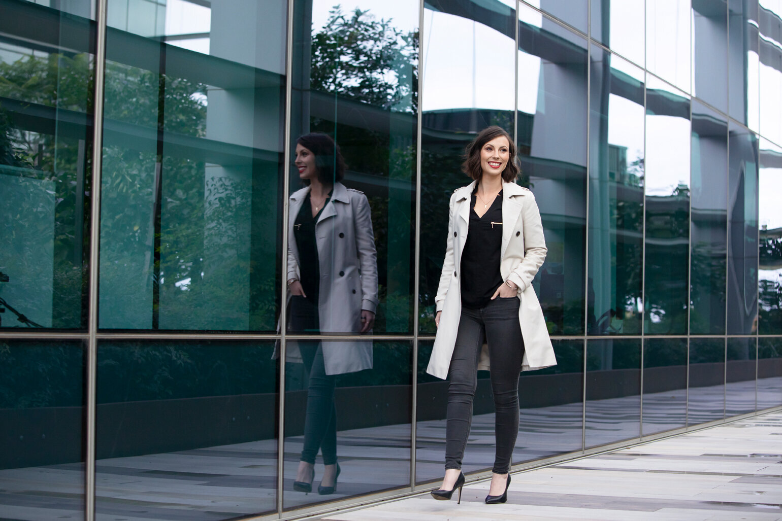 Business woman in trench coat walking next to  building windows