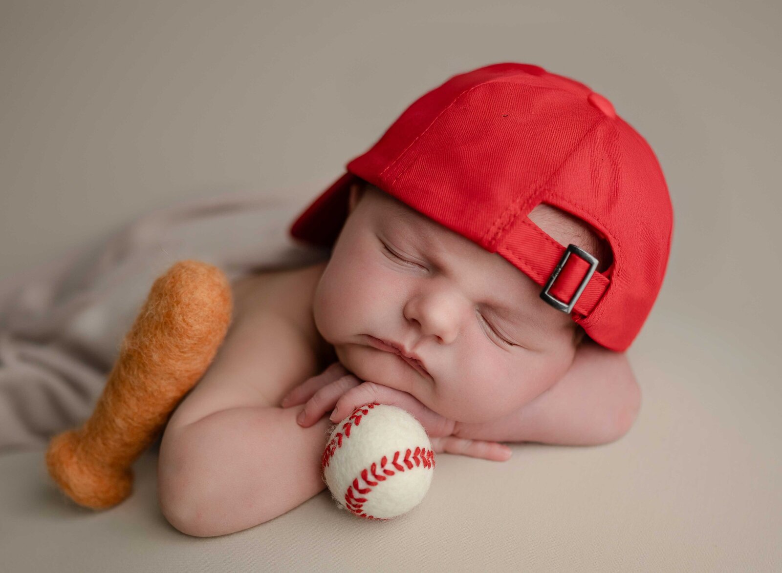 Baby boy sleeping on hands, holding felted baseball with red cap on. Photographed at Atlanta baby studio.