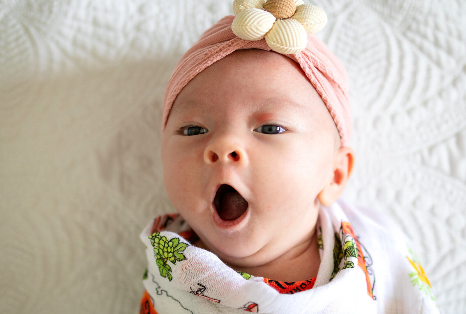 Newborn baby girl yawning while wrapped in colorful muslin, documented by San Francisco newborn photographer.