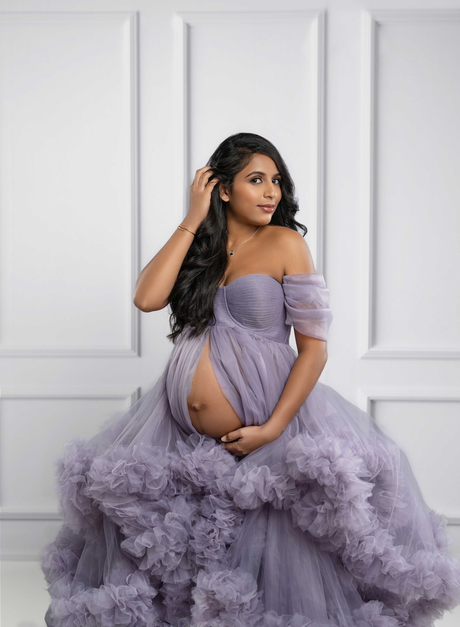 Pregnant women in Lavender maternity dress holding hair back with one hand and holding baby bump with another.