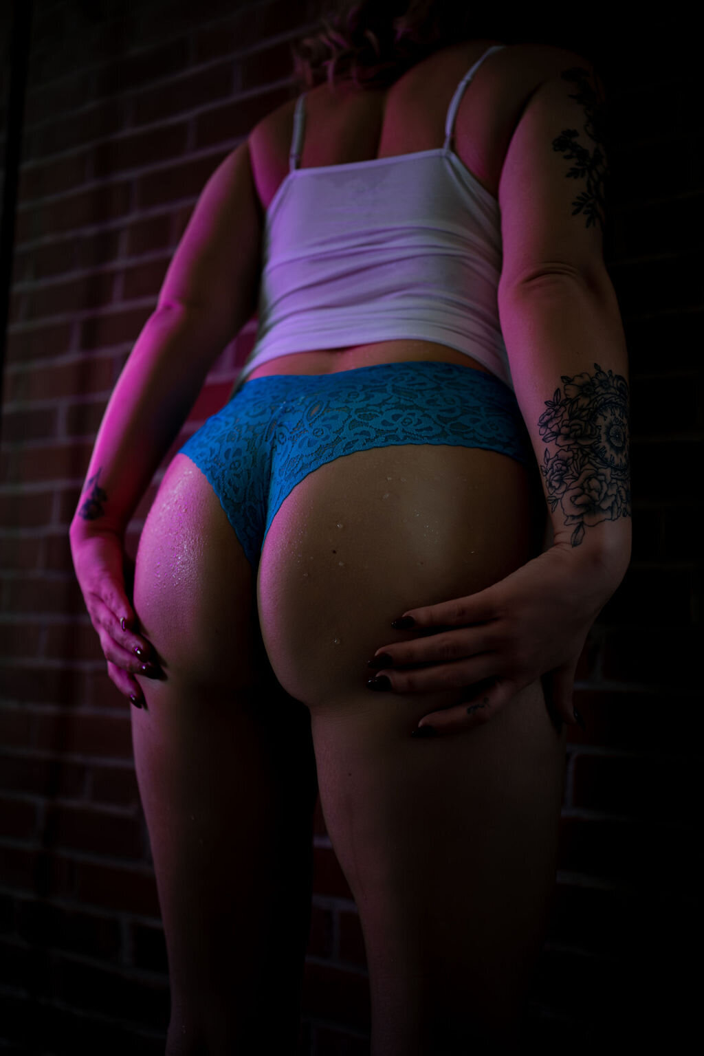 close up boudoir butt photo of woman in blue underwear and white tank top leaning against brick wall