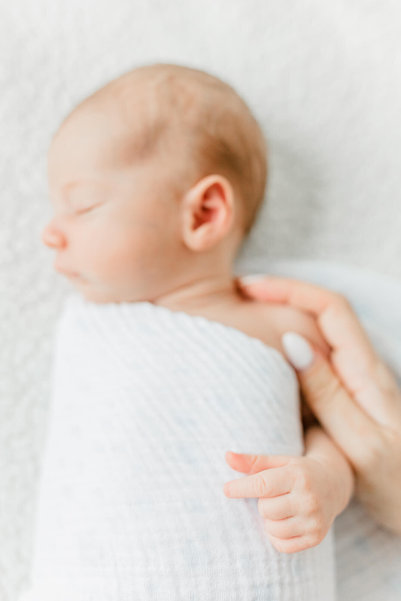 Detail image of newborn's hand with mom's hand gently holding his shoulder