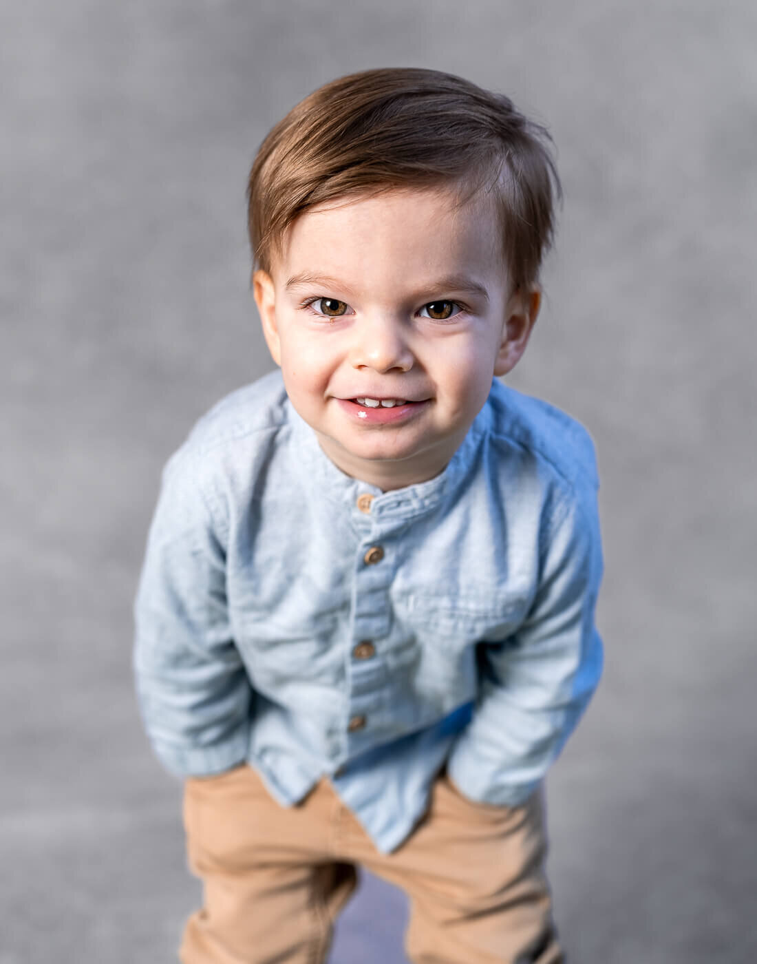 A child leans forward with their hands in their pockets, smiling.