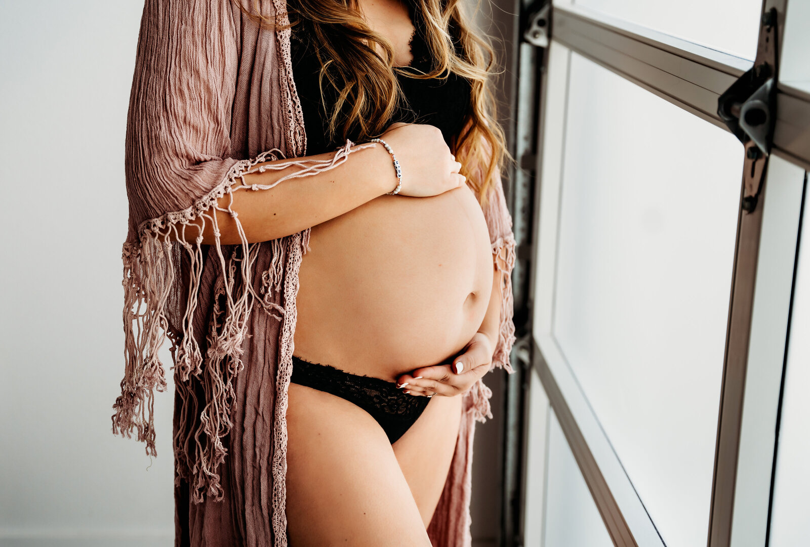 Maternity Photographer, a pregnant woman places a hand above and beneath her belly, she wears a bikini and shawl