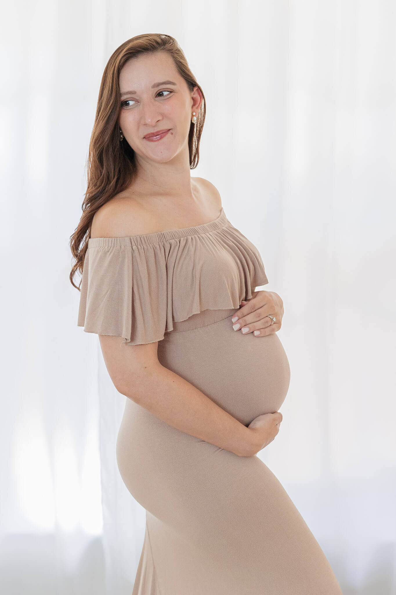 A pregnant woman in a tan dress hugging her belly in a Gainesville studio.