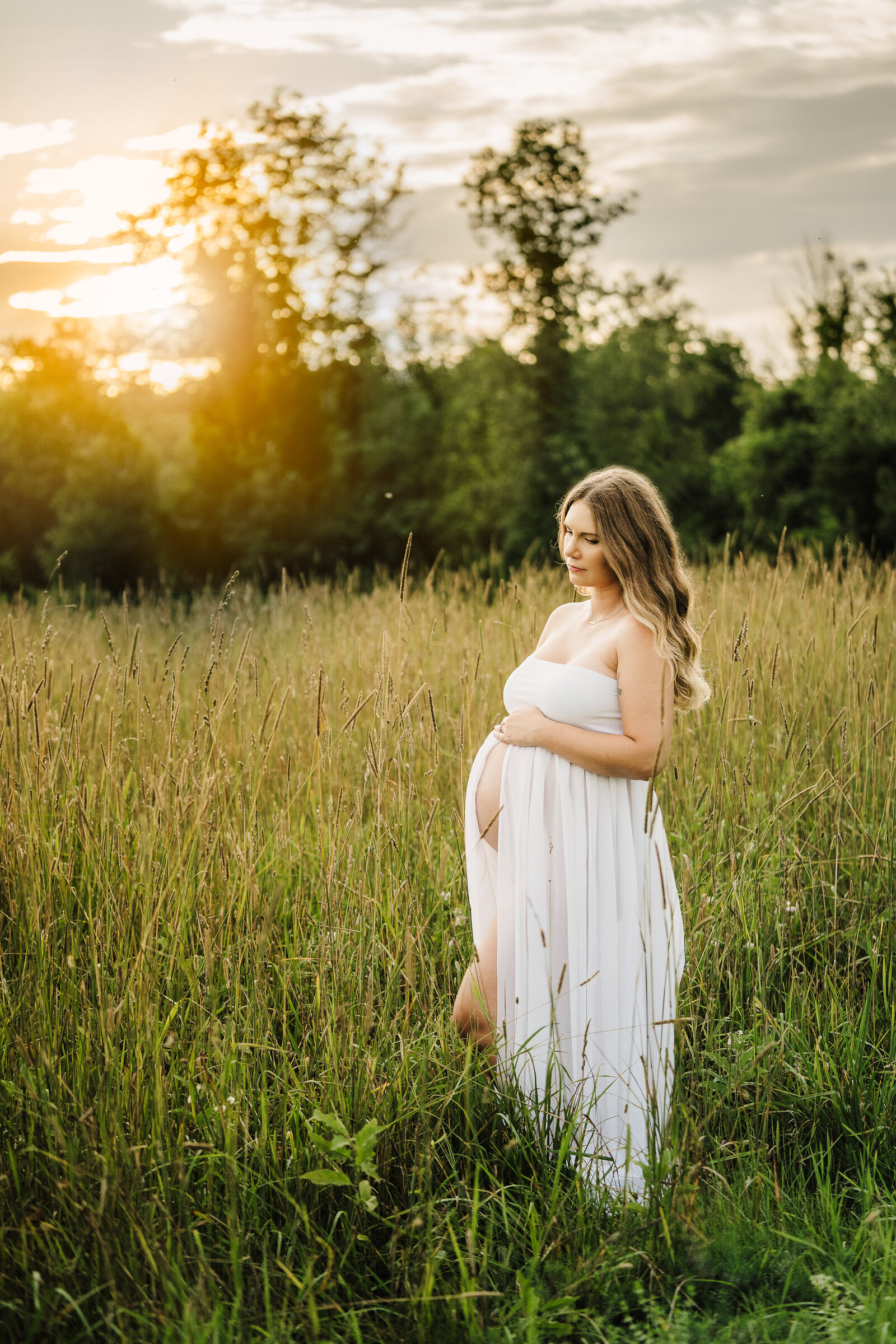 pregnant woman in white dress looks at belly