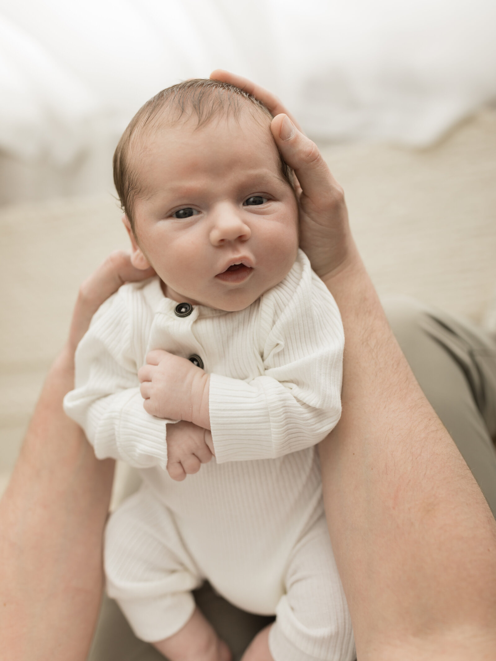 newborn baby boy in white outfit laying in dads lap for studio portraits cleveland newborn photographer