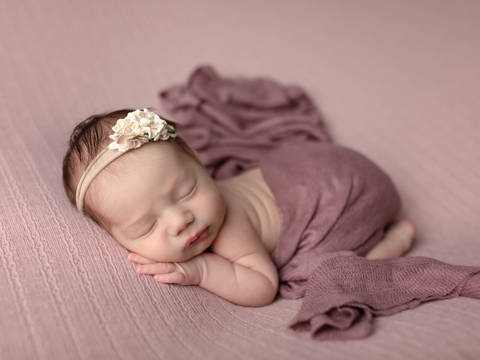 newborn baby girl laying on pink fabric for photoshoot