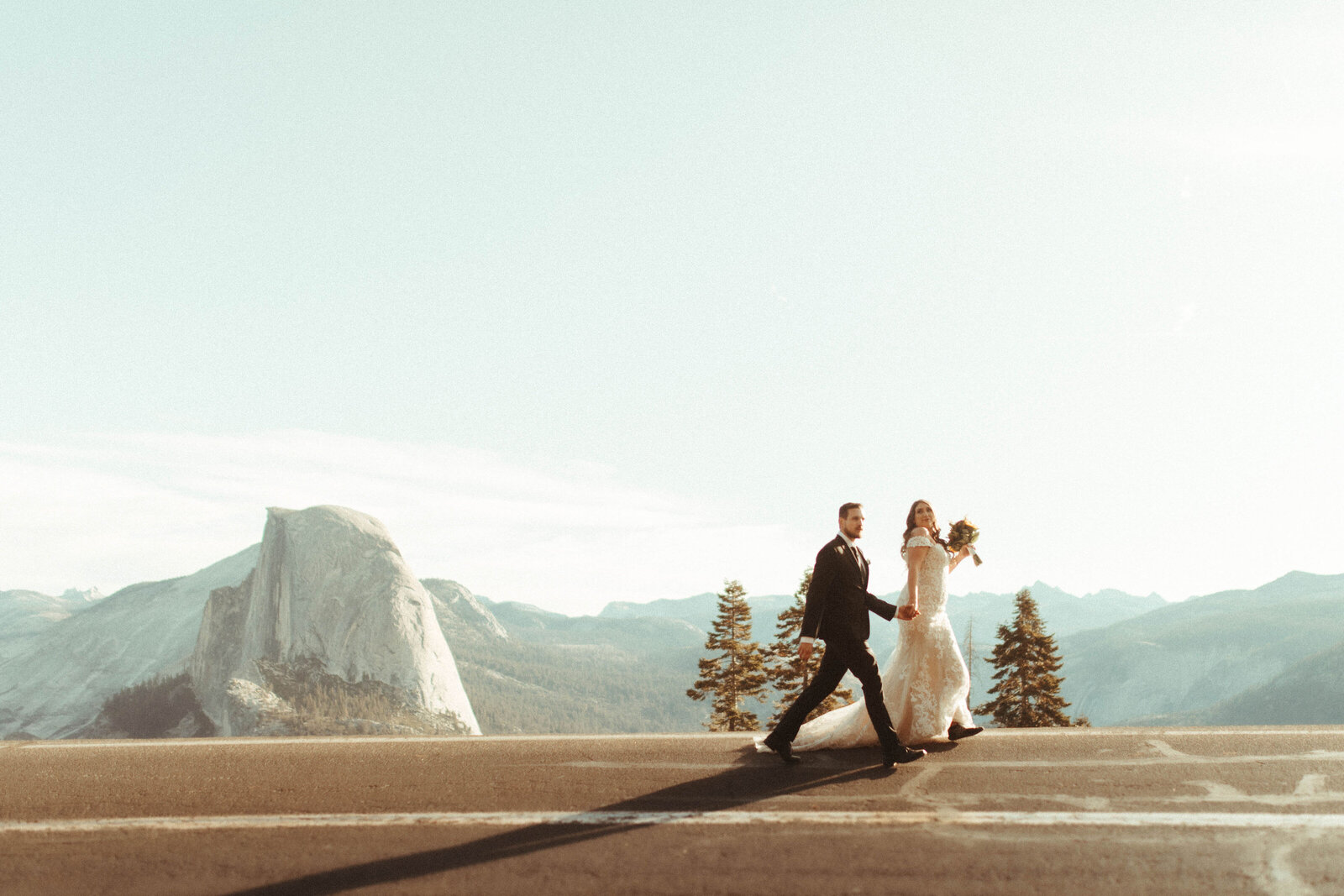a bride and groom running together on a road in the mountains