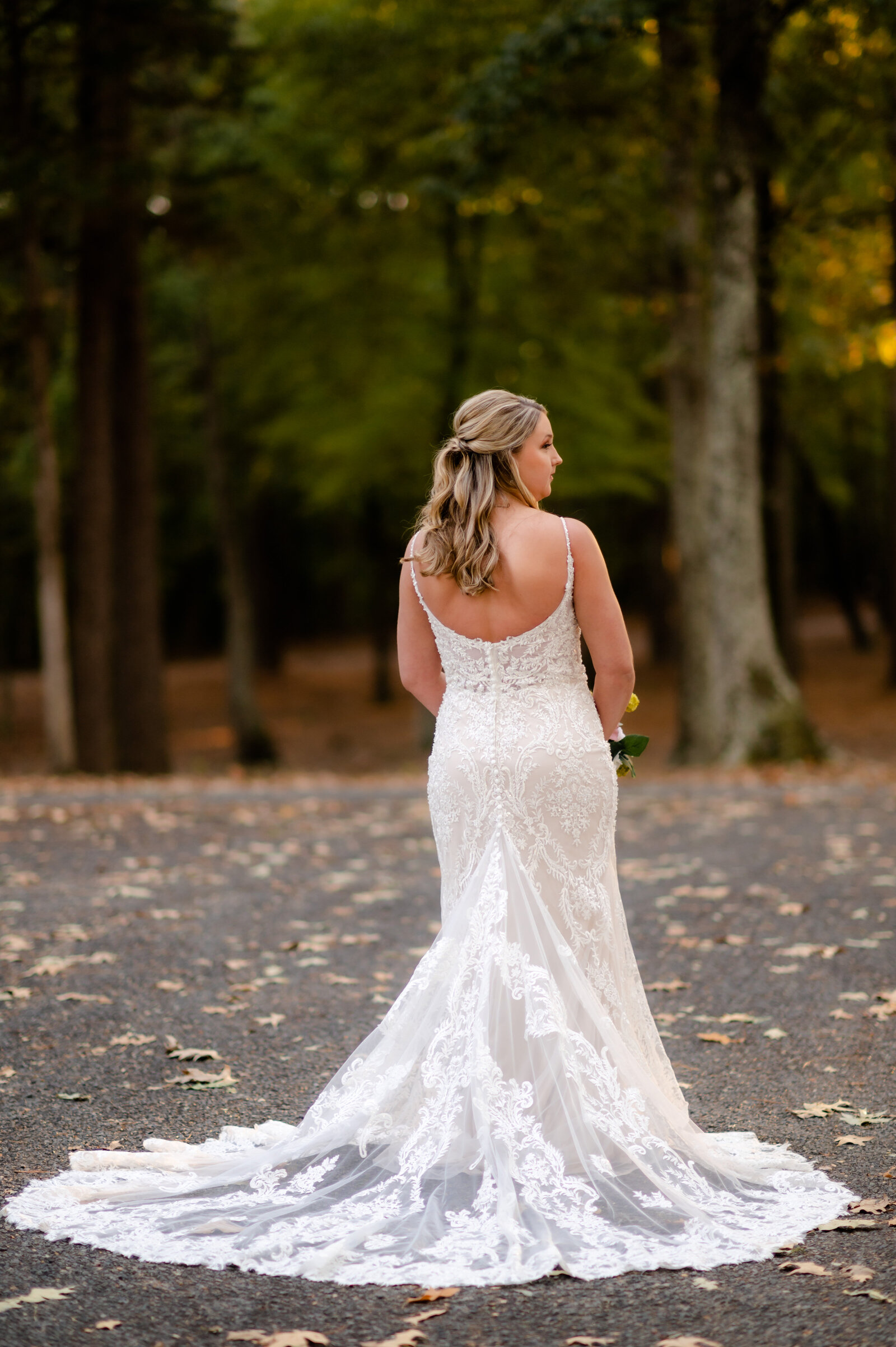 fall wedding with bride standing amoungst fallen leave with her back to the camera to show off her lace wedding dress train caputerd by best little rock ar photographer