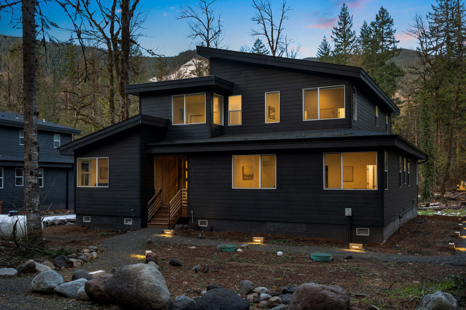 Front view of a dark modern cabin at dusk with warm lighting
