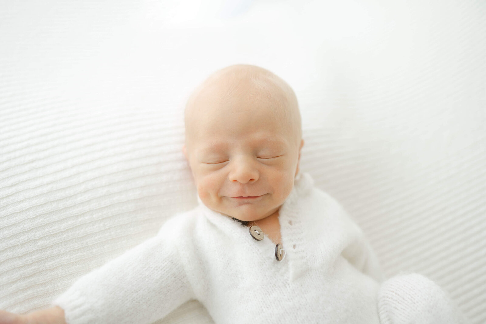 newborn baby boy smiling as he sleeps with a precious cheek dimple