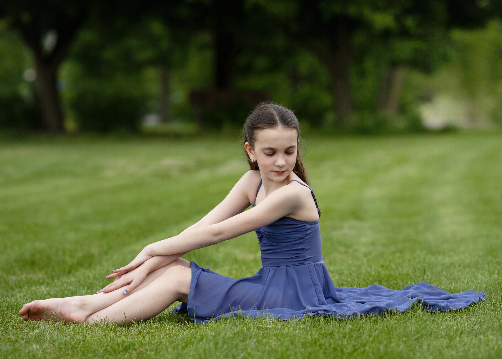 Girl in blue dance dress sitting in grass, looking over her shoulder.