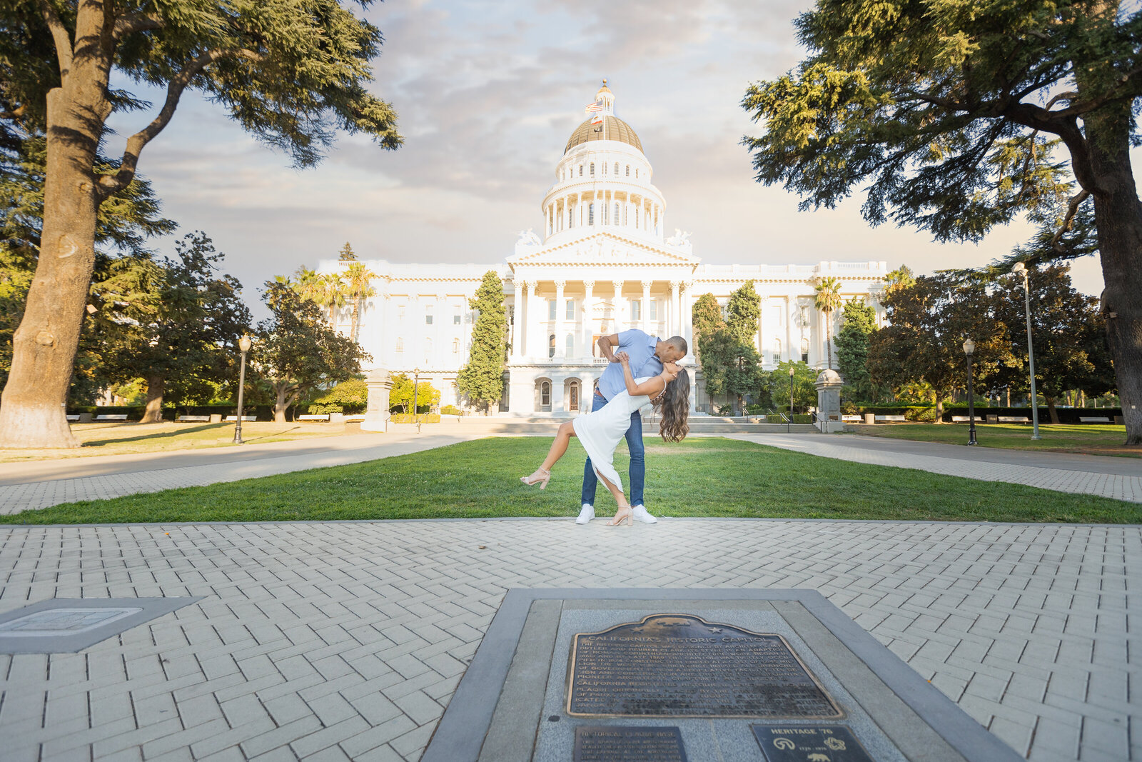 engagement photo in front of sacramento capitol building with engaged couple dipping for a kiss. photo be wedding photographer sacramento, philippe studio pro