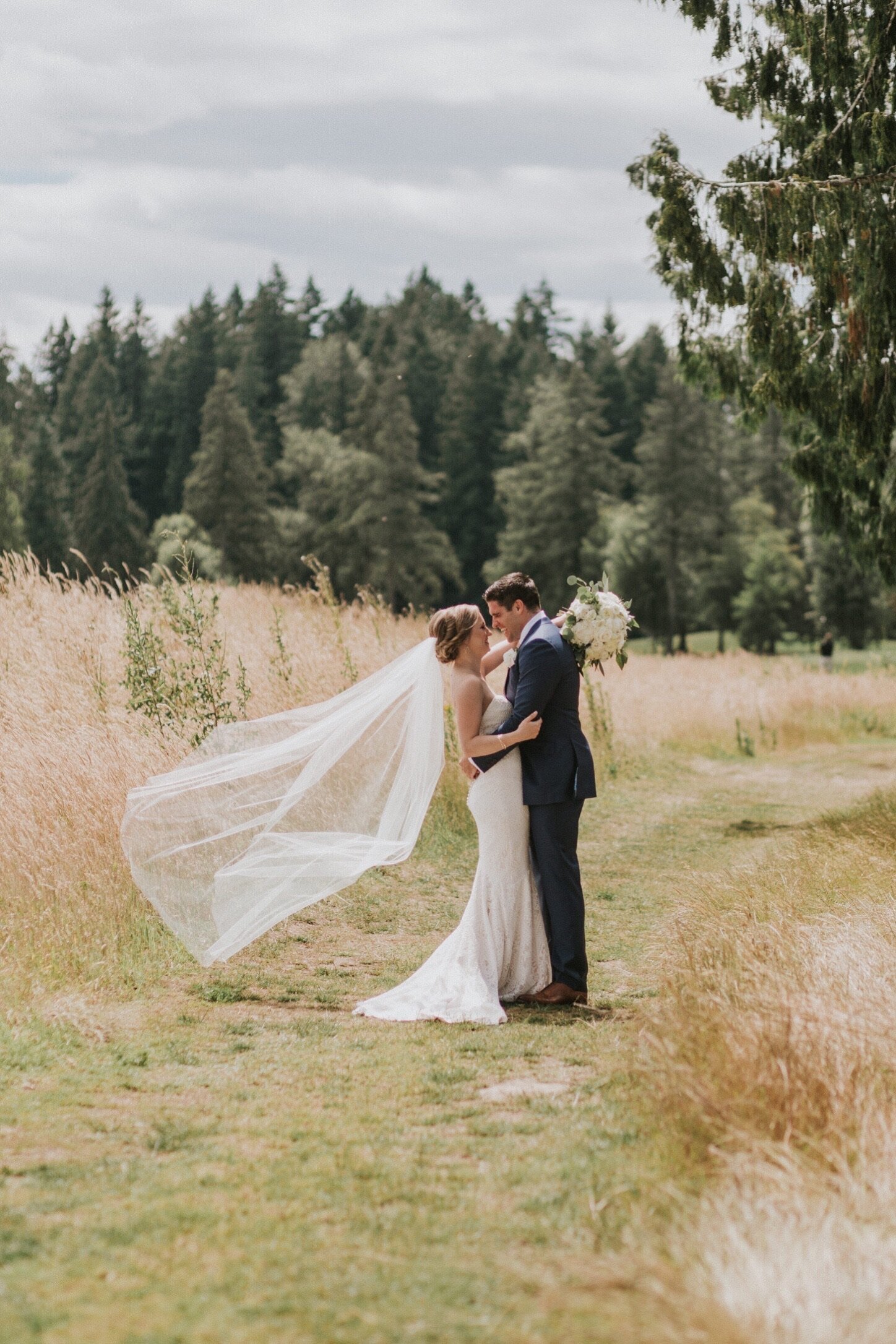 Real bride and groom with a blowing veil and standing in a field