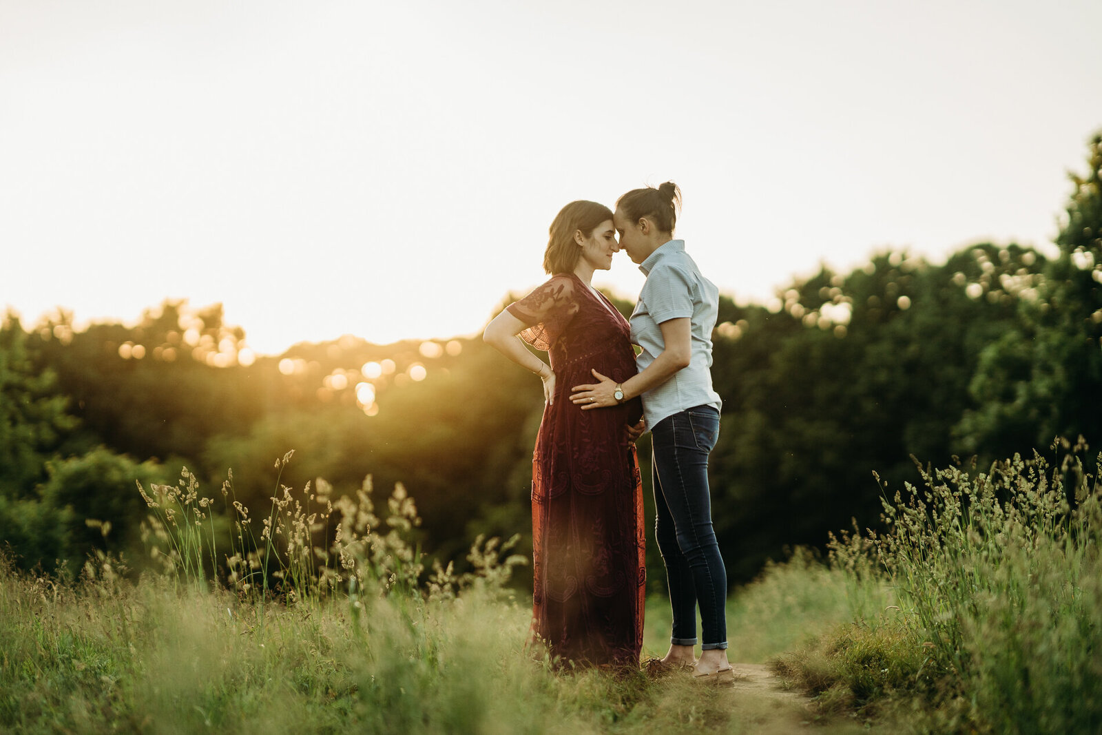 pregnant couple stands forehead to forehead in boston field at sunset