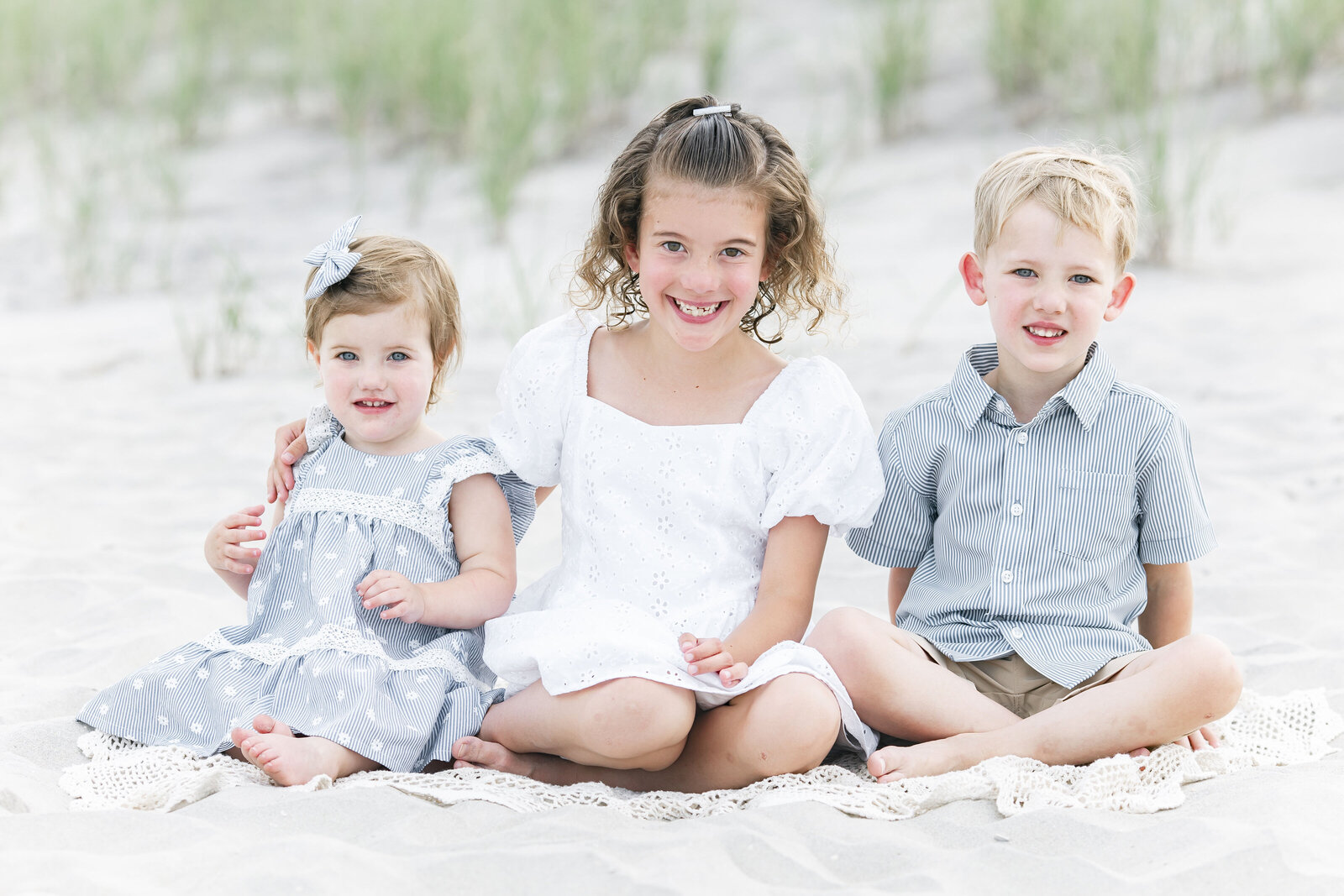 three siblings sitting next to each other on beach smiling for photo for ally kimpton 