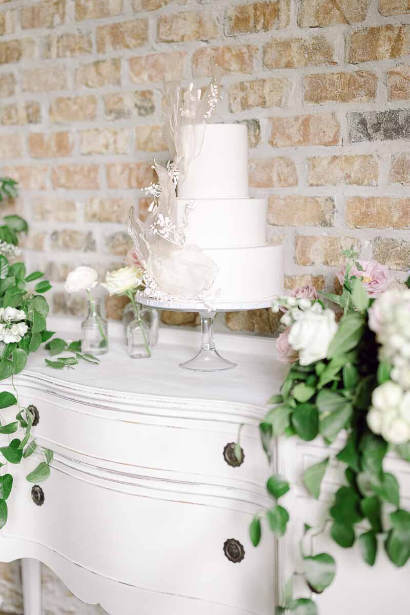 photo of wedding cake sitting atop rustic white dresser surrounded by flowers