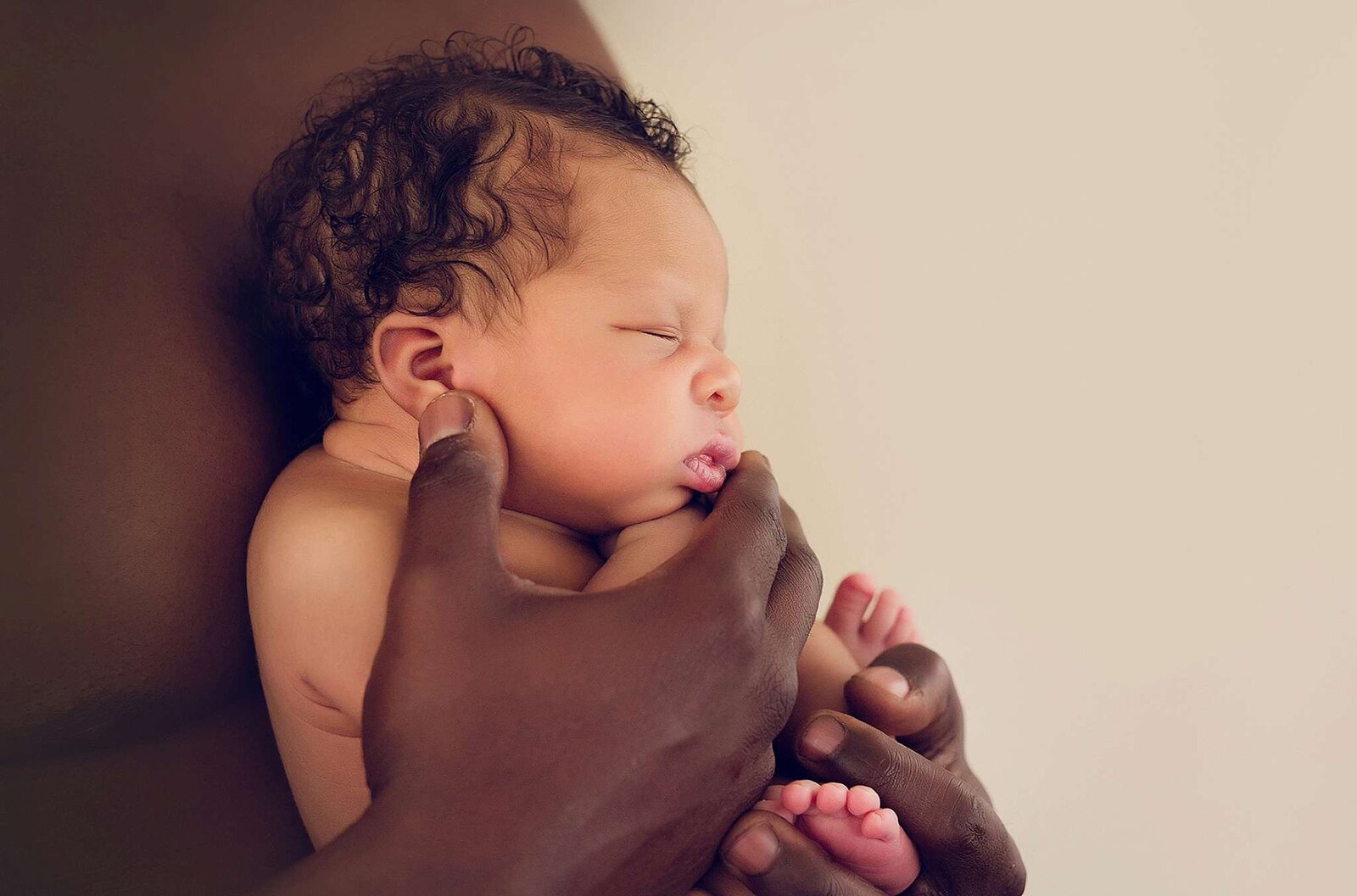  A black man lovingly holds his baby in his arms, captured during an in-home newborn session by Bia Schaefer Photography.