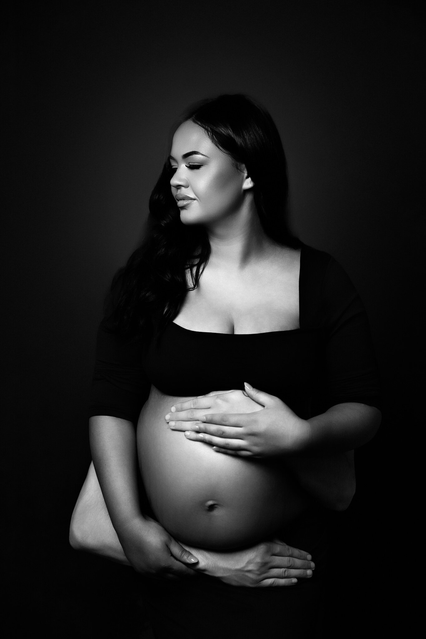 strong black and white image of mumma holding her pregnant belly with her partners arms supporting her 