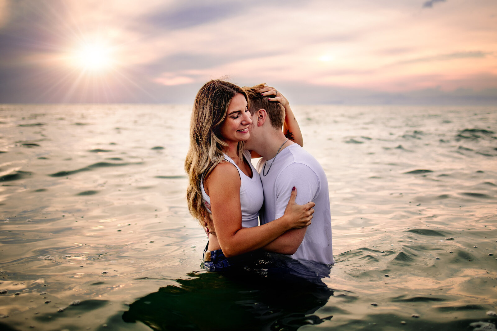Man snuggles up with his fiancé kissing  her neck while swimming in the water at Presque Isle
