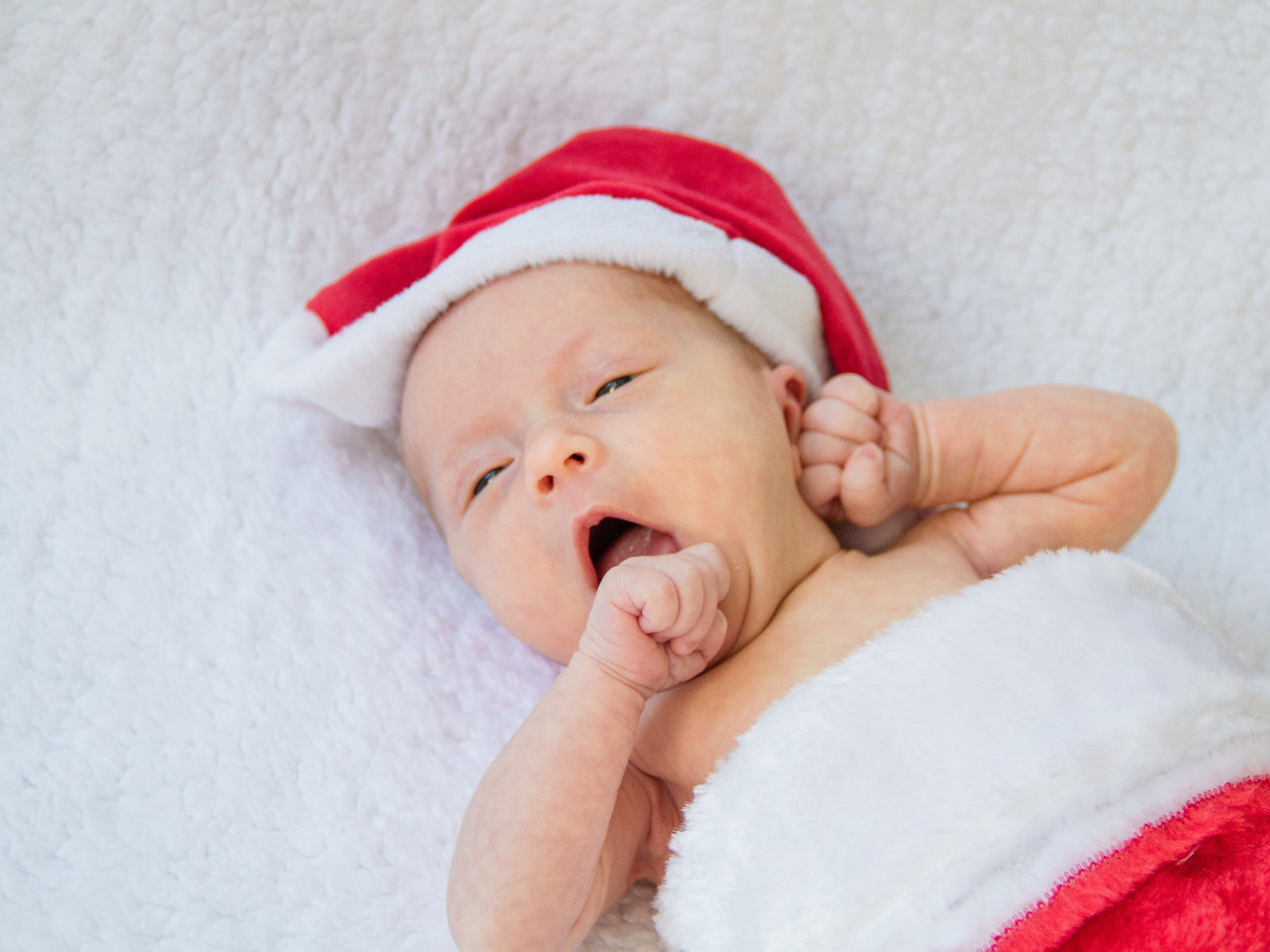 Newborn infant yawns in her Santa hat, in a Christmas stocking