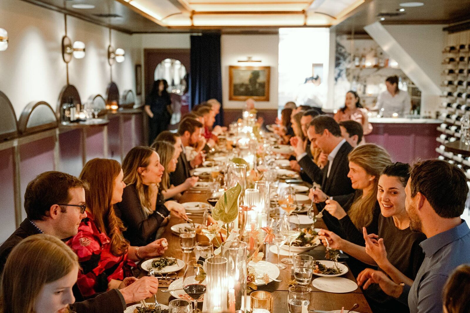 Candlelit wedding dinner at an intimate restaurant with guests gathered around a long table, enjoying conversation and wine.