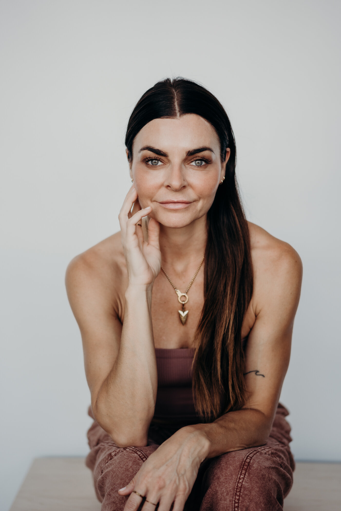 A striking portrait of an aesthetician, thoughtfully, looking at the camera with long, dark brown hair and big blue eyes.