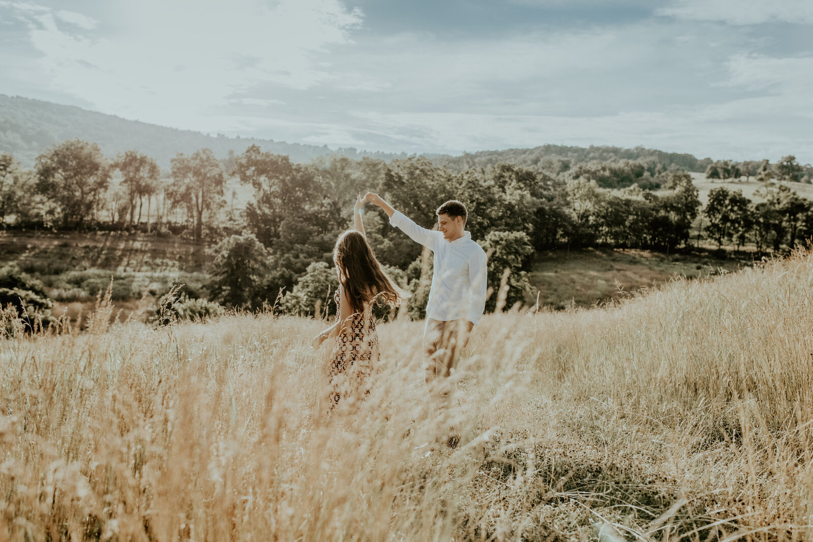 A young couple dances in a golden field at sunset