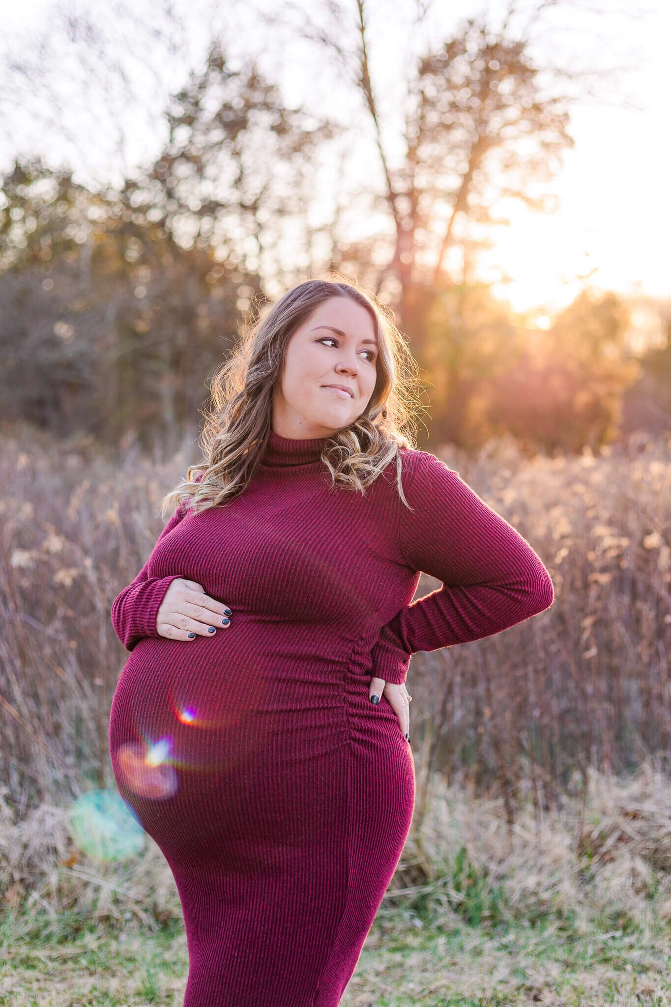 A mother-to-be in a red dress posing at a park at sunset.