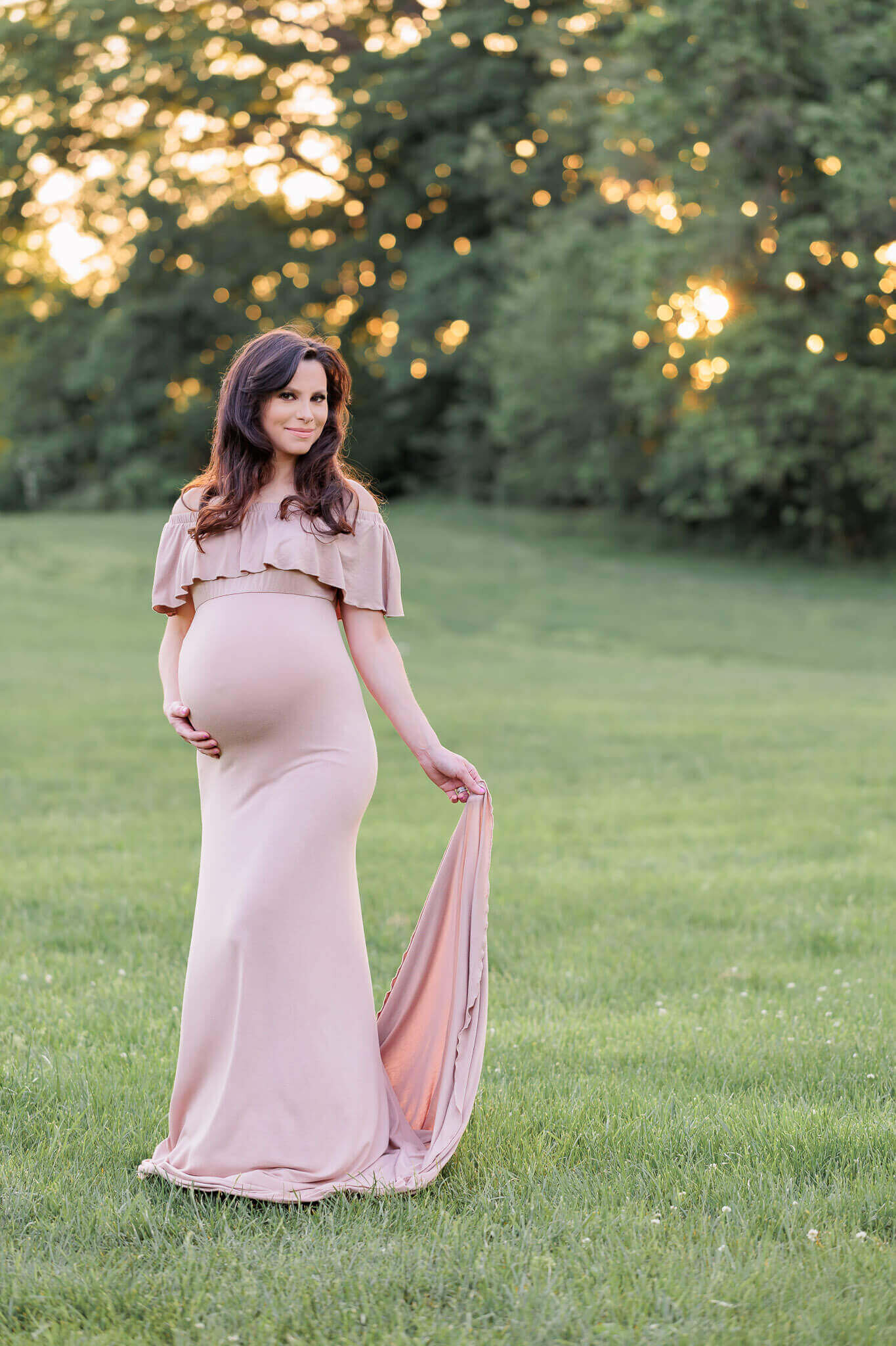 A beautiful woman in a tan dress posing at a park at sunset for her Burke maternity photos.