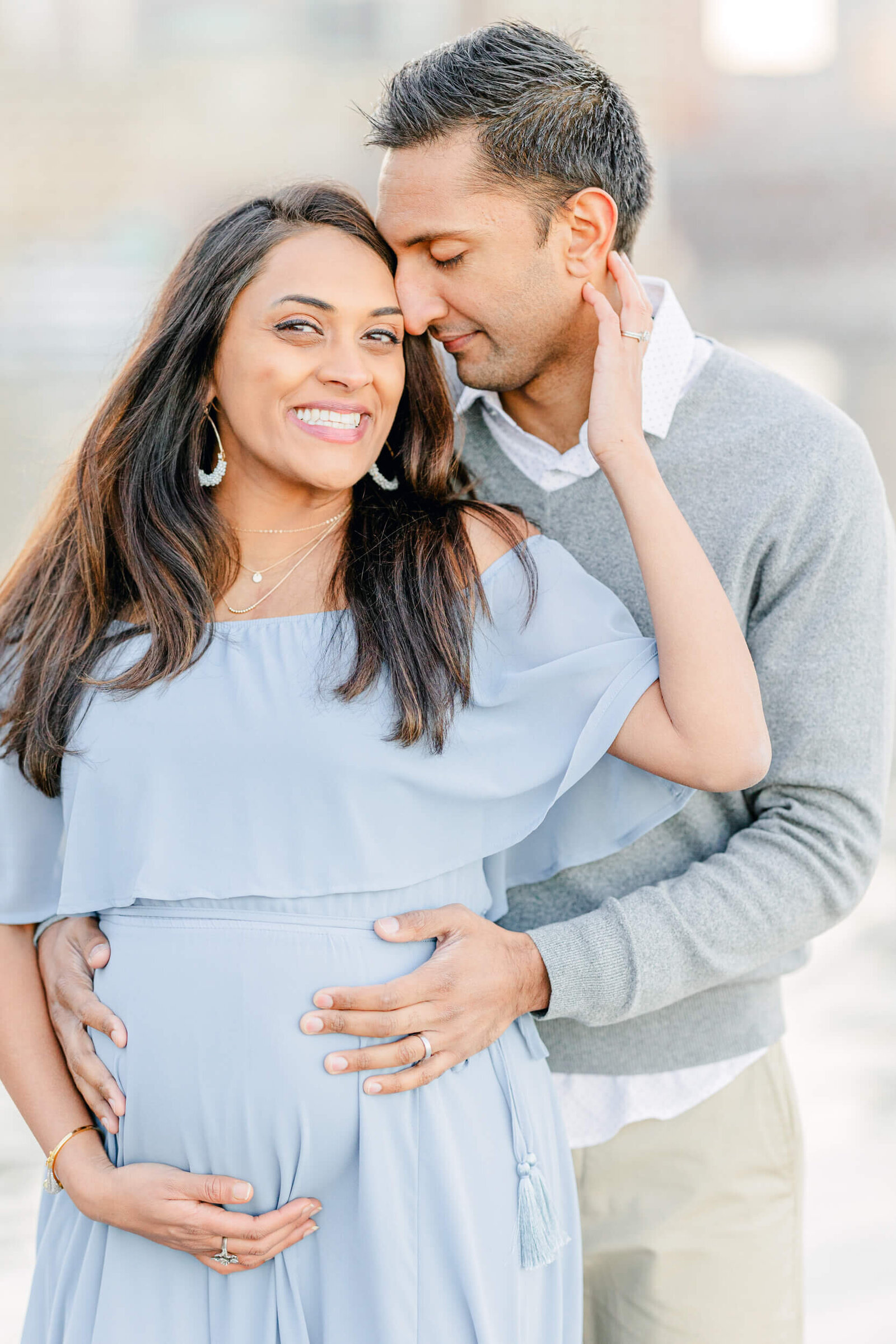 Pregnant woman smiles as her husband leans in and holds her baby bump