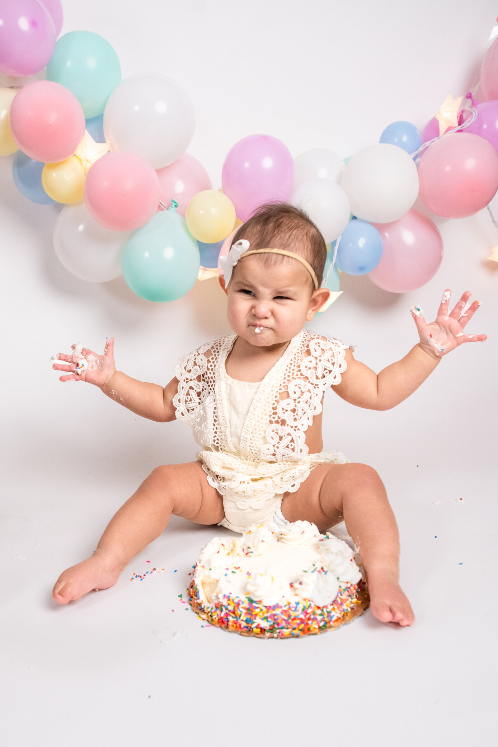 baby with sprinkle birthday cake and balloon garland