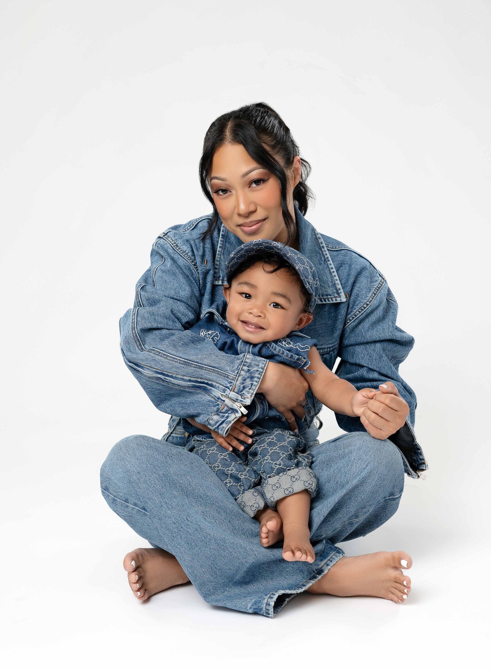 Mom sitting on white backdrop floor with baby on her lap and cuddling him.