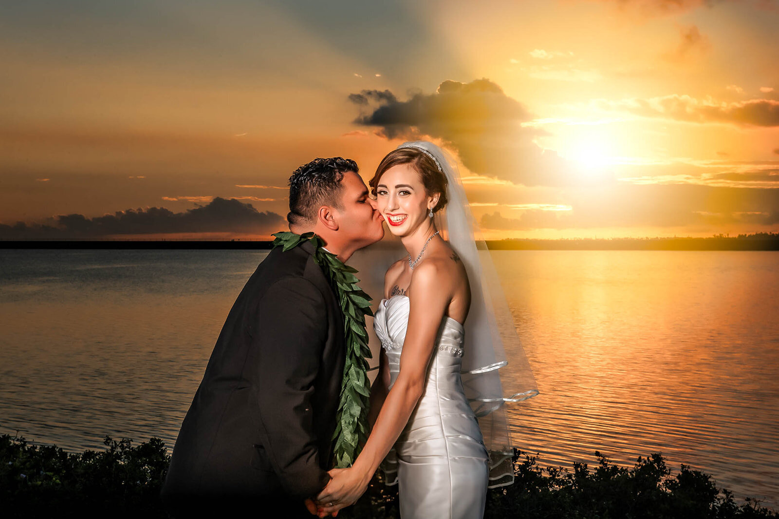 A romantic moment as the bride and groom share a kiss at sunset by the beach, captured by CMH Studios during a destination wedding