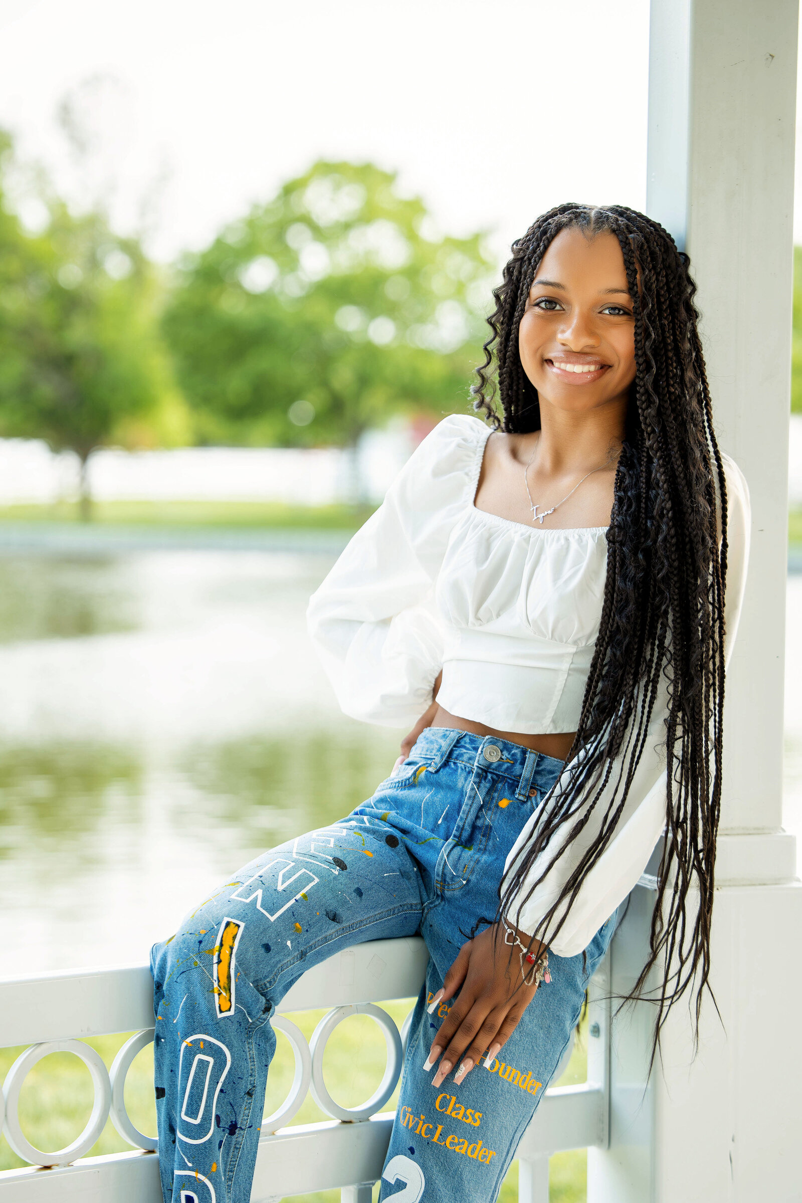 Senior girl in white top and designed blue jean pants sitting on rail on a gazebo