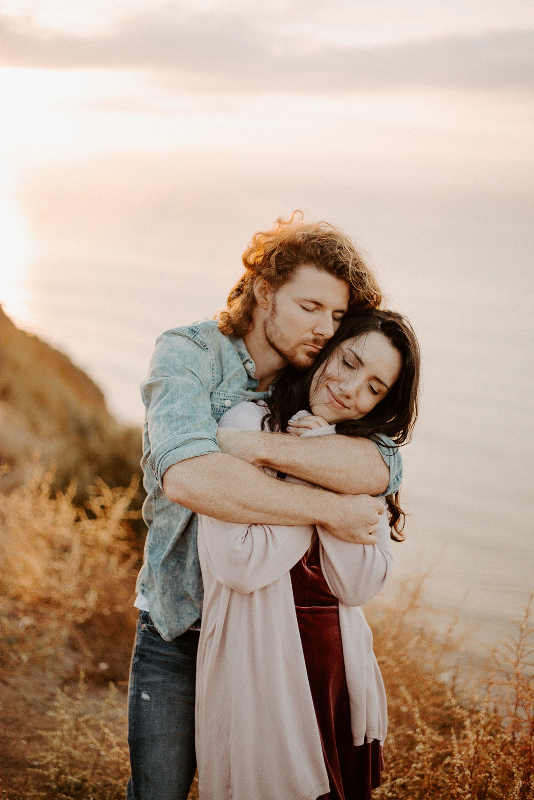 Man hugging his wife from behind next to the ocean during their California Engagement Session