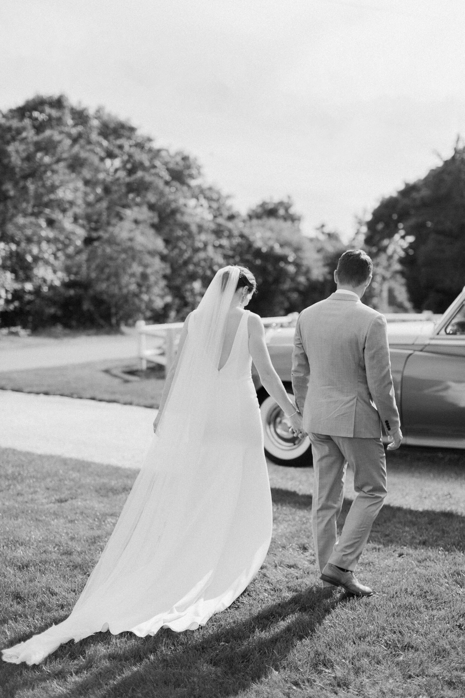 Black and white photo of a couple holding hands and walking towards a car.