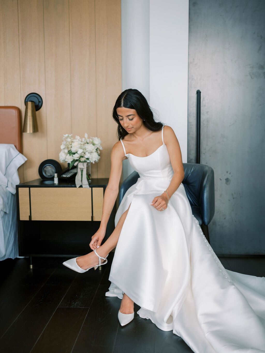 Bridal portrait putting on shoe with bouquet in the background.