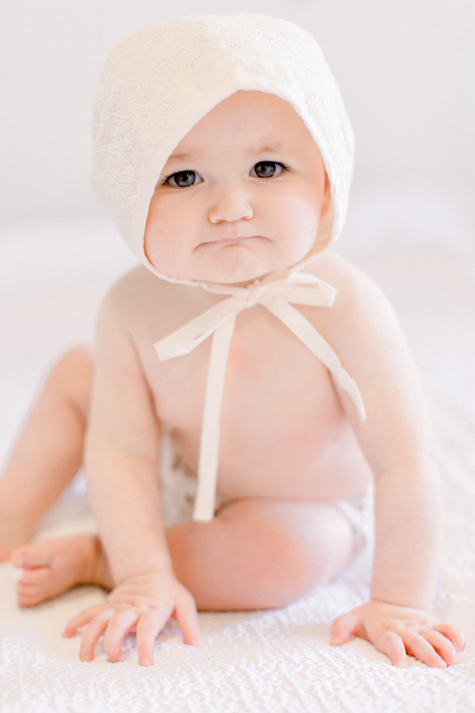 6 month old baby in a lace bonnet in a neutral studio looking inquisitively by NH newborn photographer Fieldstone Studio.