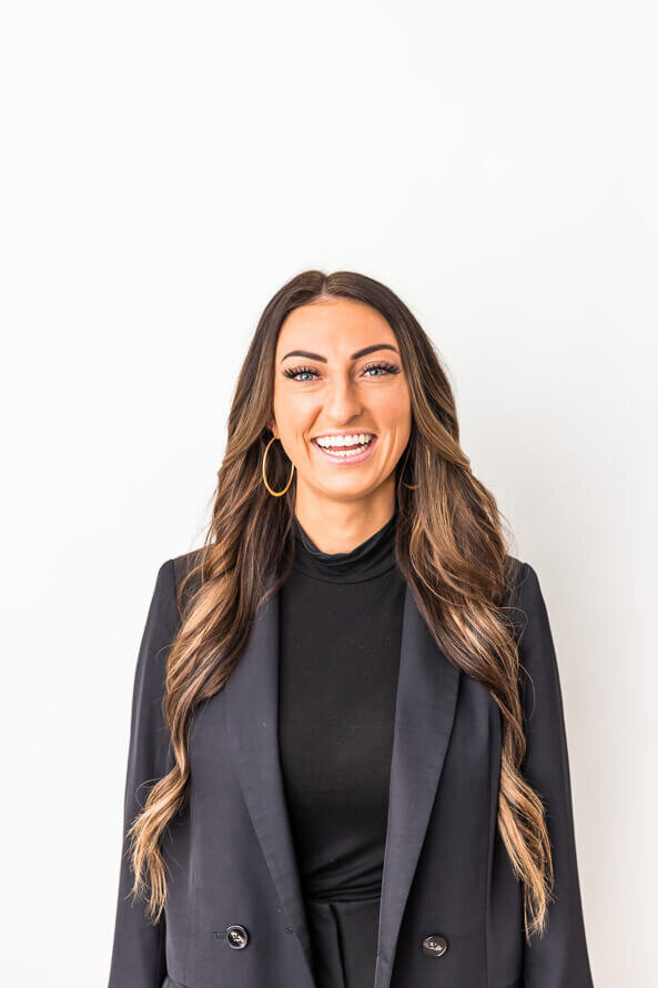 Woman in gray jacket smiles largely in front of a white backdrop.