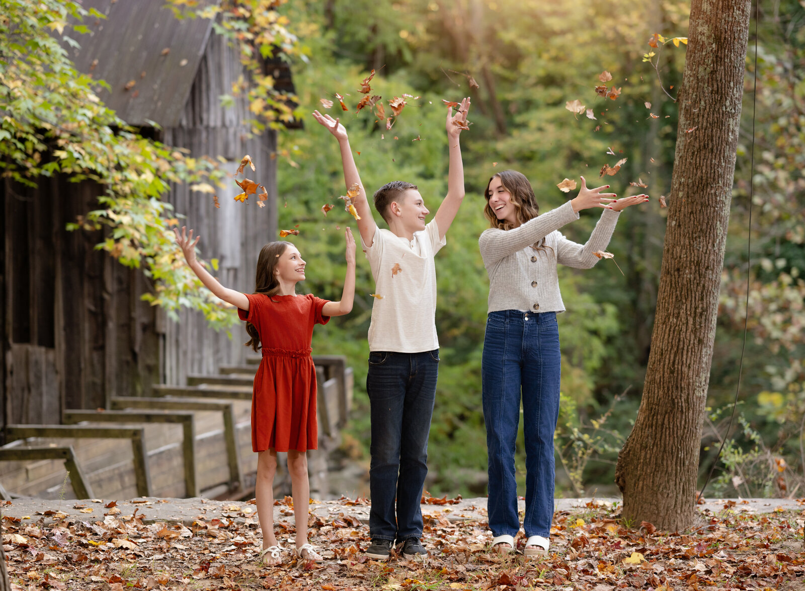 Kids standing in woods and throwing fall leaves in air. Photo taken by Atlanta Family Photographer.