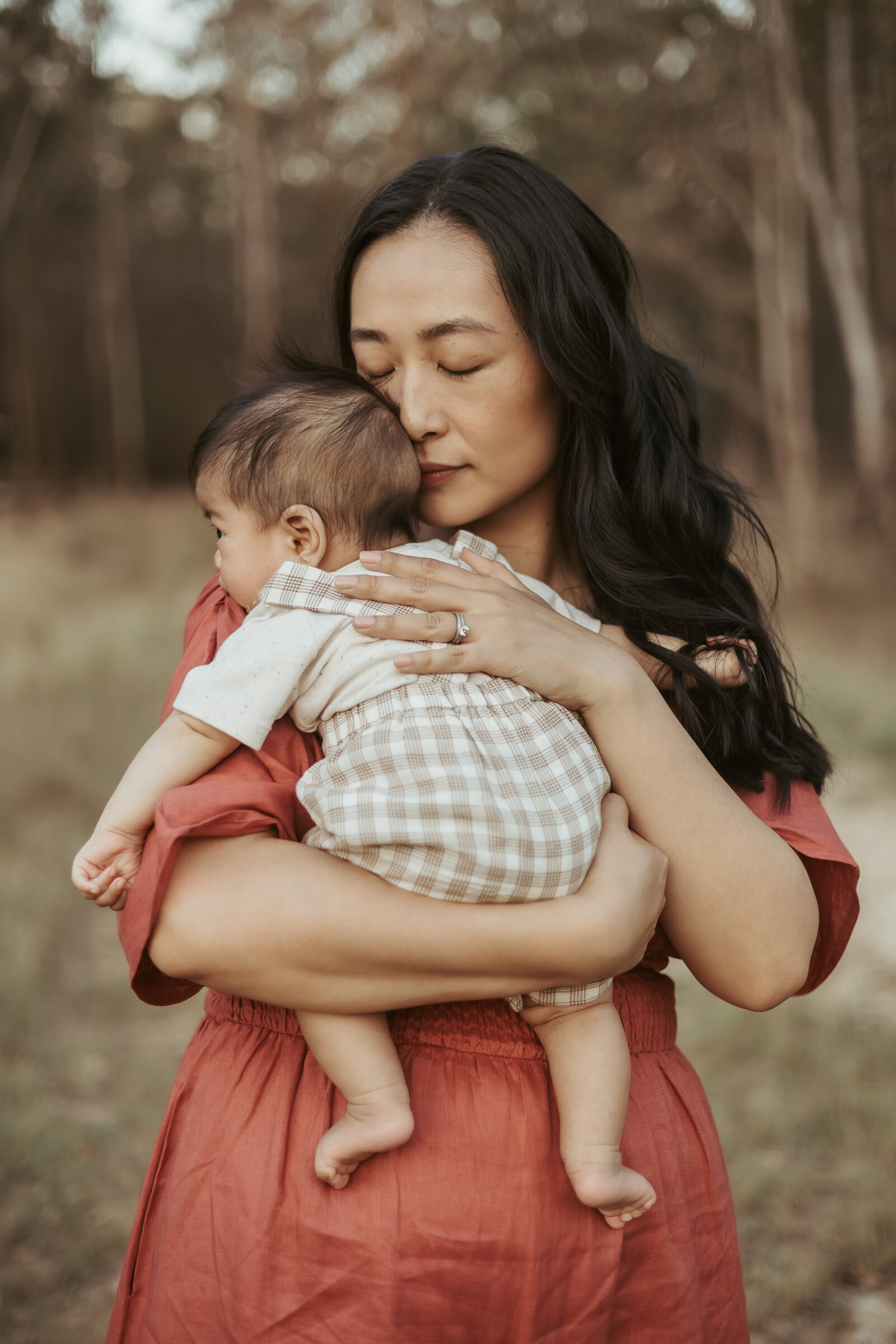 Mum has her eye closed as her holds her baby close and breathes him in for this special memories during her outdoor family photo session.