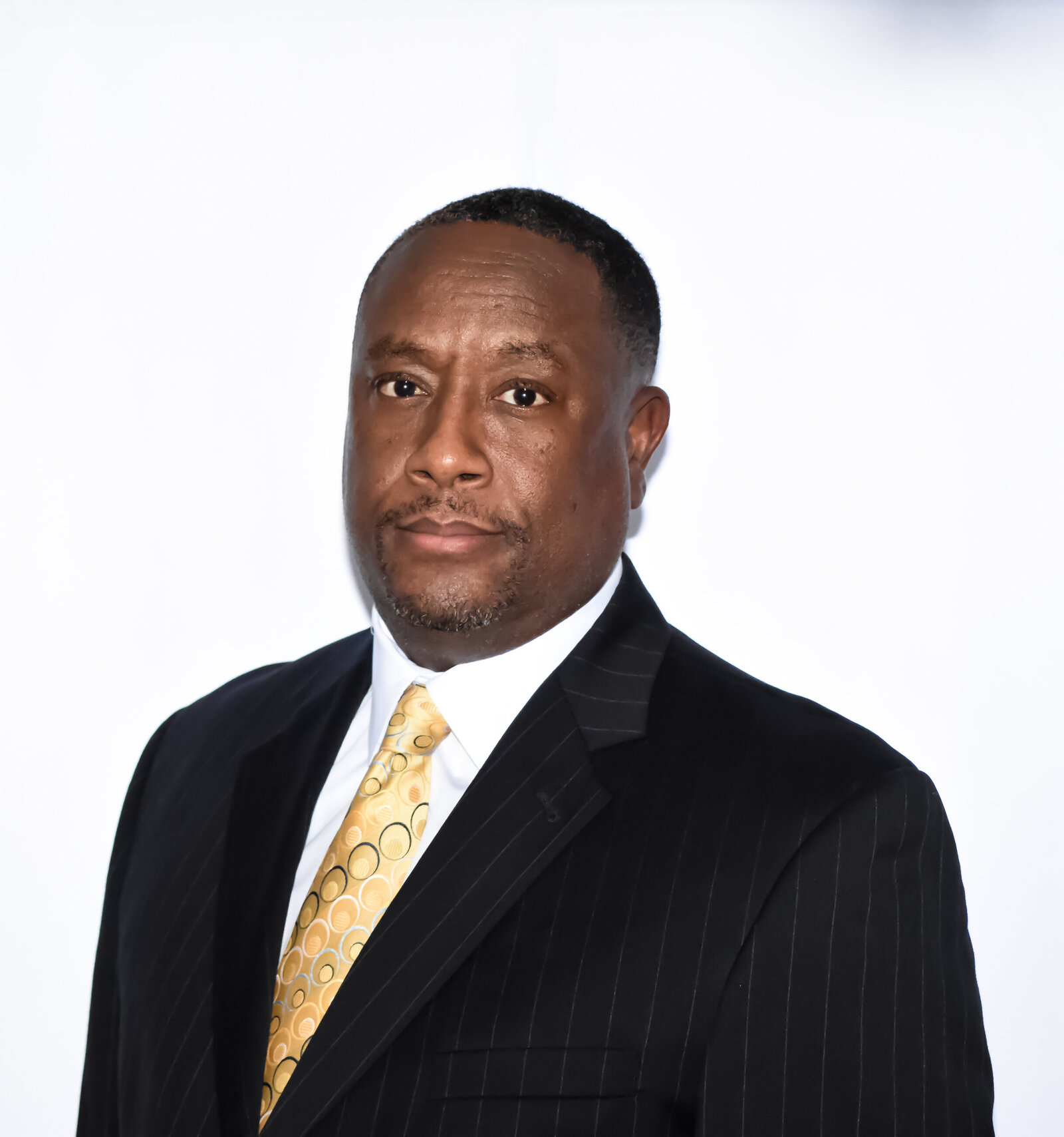a man dressed in a black suit jacket with a yellow tie posing for his headshot photographed by Millz Photography in Greenville, SC