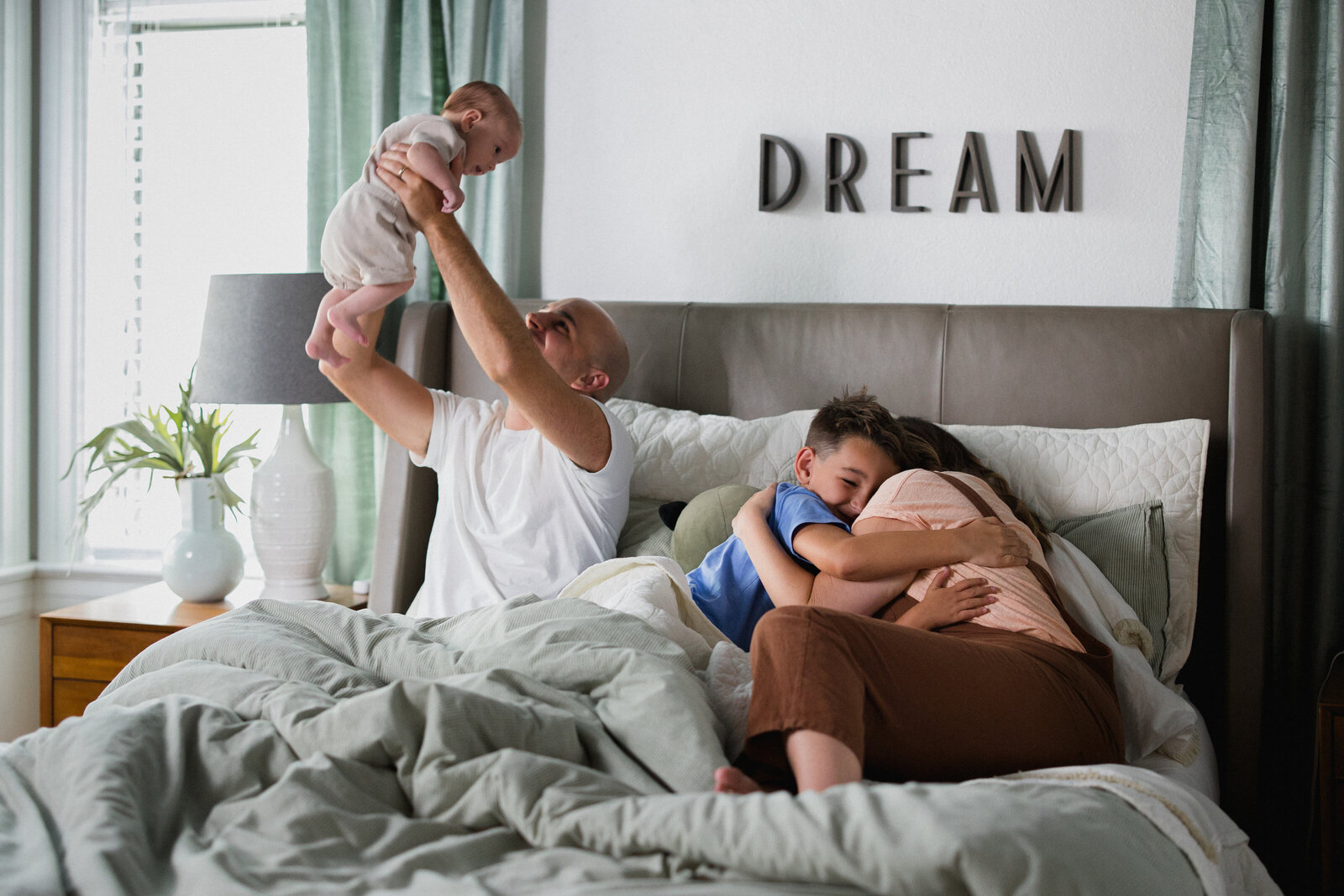 Dad holds up baby while mom snuggles with two younger boys in bed at home in Lakeland