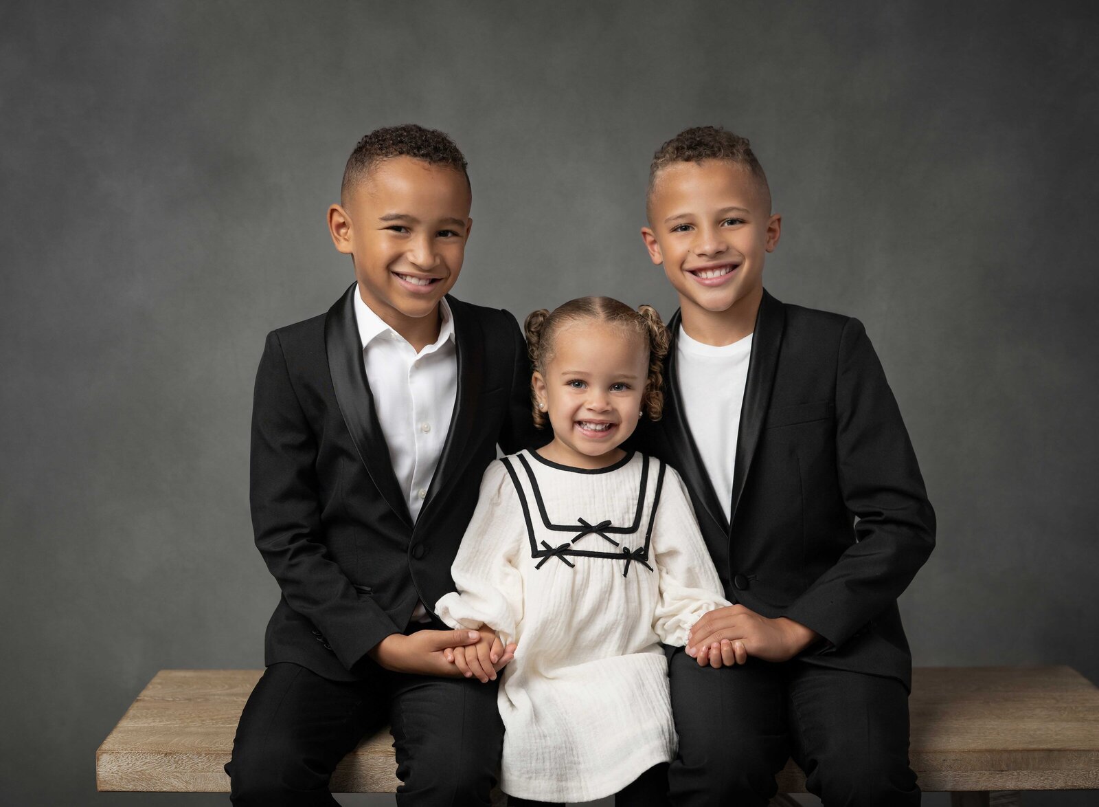 Siblings sitting on bench and taking professional photo. Family photo taken at Atlanta Photo Studio by Jenni Nikki Photography.