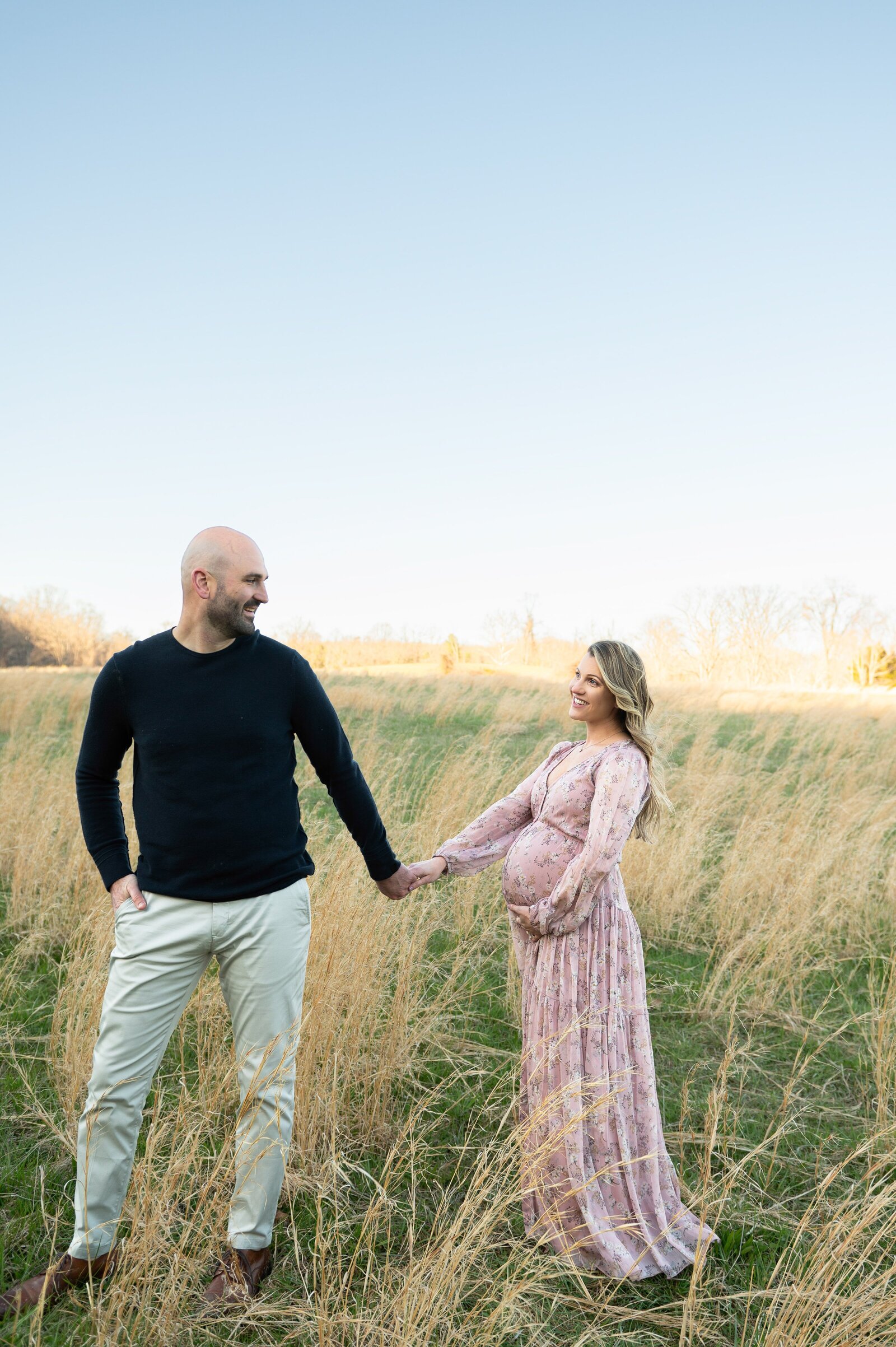 husband leading pregnant wife through a field
