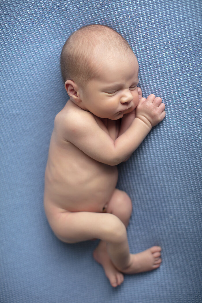 Newborn photographed from the side on blue.