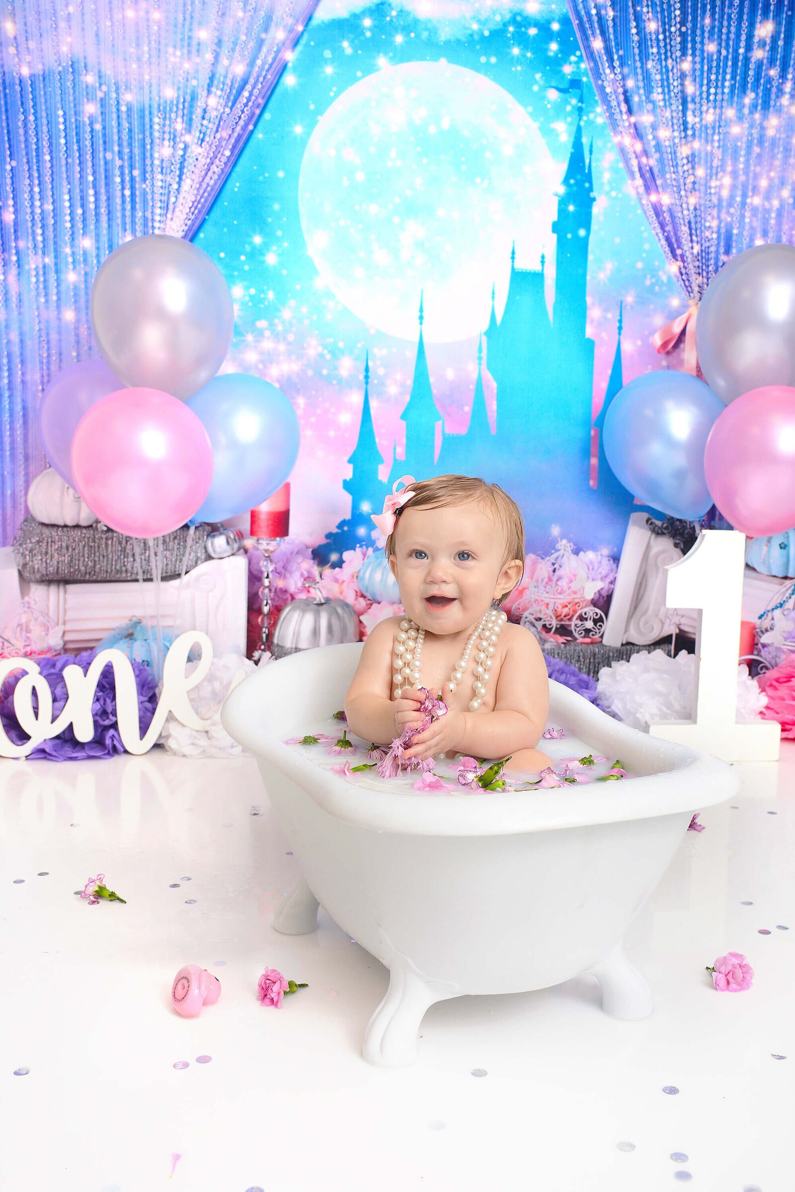 baby girl smiles in a milk bath with purple flowers and a cinderella themed background