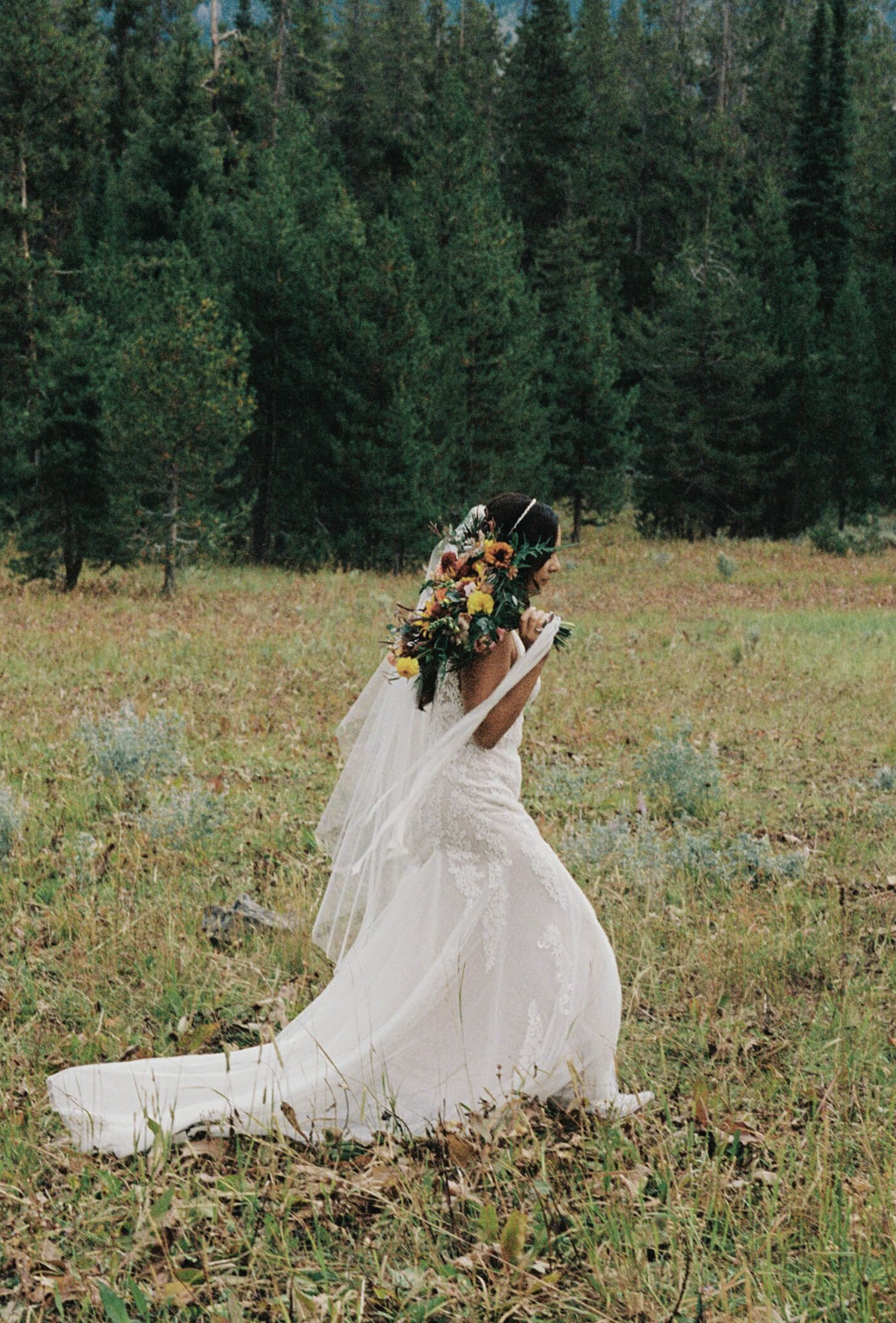 Bride carrying bouquet walking along grassy field